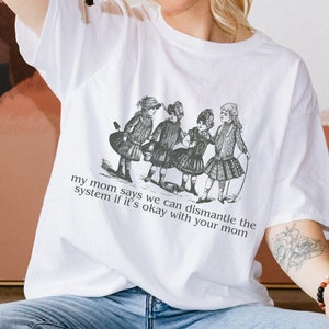 Puede incluir: Camiseta blanca con una ilustración en blanco y negro de cuatro niños jugando. El texto en la camiseta dice "my mom says we can dismantle the system if it's okay with your mom".