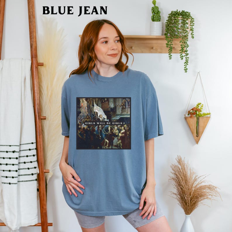 May include: A blue t-shirt with a graphic of a painting featuring a group of people and the text "Girls Will Be Girls".