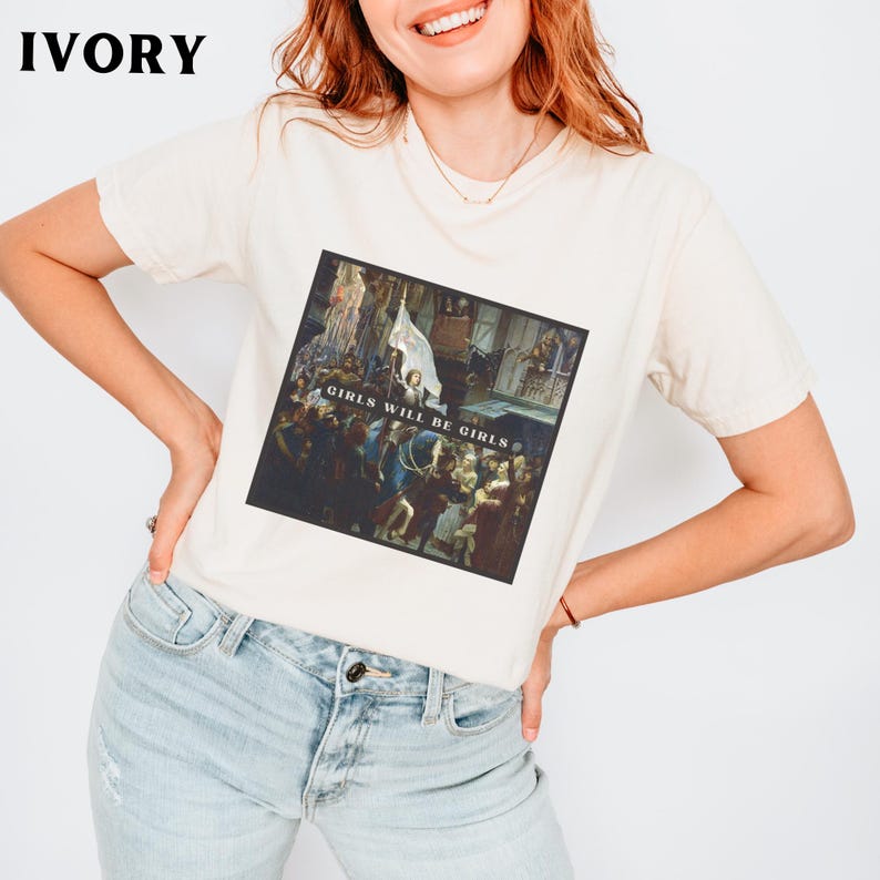 May include: A white t-shirt with a graphic print of a painting. The painting depicts a group of people in a historical setting. The text "Girls Will Be Girls" is printed on the shirt.