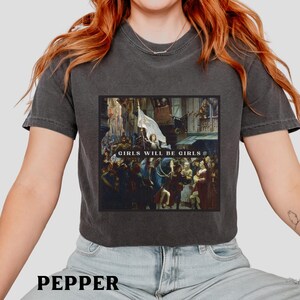 May include: A charcoal gray cropped t-shirt with a graphic print of a painting. The painting depicts a group of people in a historical setting. The text "Girls Will Be Girls" is printed on the graphic.