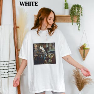 May include: White oversized t-shirt with a graphic print of a painting. The painting depicts a group of people in a street scene. The text "Girls Will Be Girls" is printed on the shirt.