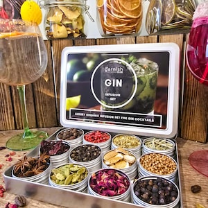 Puede incluir: Un juego de infusión de ginebra con una variedad de botánicos en pequeñas latas, incluyendo granos de pimienta, bayas de enebro y cítricos secos. El juego se presenta en una bandeja de metal con una caja que dice "GIN INFUSION SET".