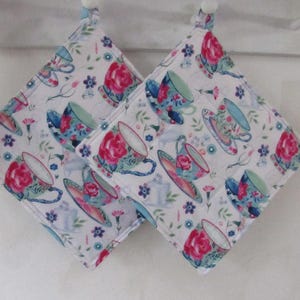 May include: Two white cotton pot holders with a floral pattern of teacups and flowers in shades of pink, blue, and green.