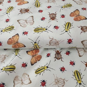 May include: White fabric with a repeating pattern of butterflies, beetles, and ladybugs in shades of brown, yellow, and red. The insects are scattered across the fabric, creating a whimsical and nature-inspired design.