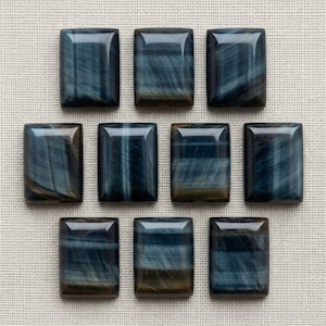 May include: Ten rectangular blue tiger's eye gemstones arranged in three rows. Each stone features a polished surface with a chatoyant, shimmering effect displaying deep blue and dark grey horizontal bands across the smooth, flat faces.