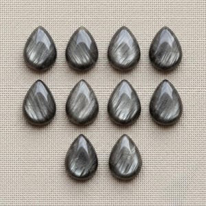 Könnte beinhalten: Zehn tropfenförmige Cabochons aus Silbersheen-Obsidian. Jeder Stein hat eine glatte, polierte Oberfläche mit einem ausgeprägten, metallisch grauen, faserigen Schimmer, der das Licht linear und gerichtet über die dunkle Basis reflektiert.