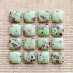 May include: Sixteen square cabochons arranged in a four-by-four grid. Each piece is a smooth, polished stone featuring a pale mint green base color with scattered, irregular deep red and magenta inclusions throughout the surface of the stones.