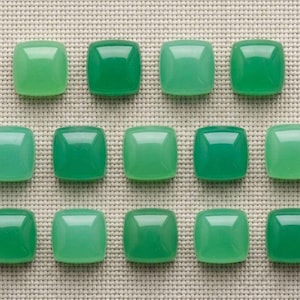 Op de afbeelding: Een verzameling van veertien gladde, vierkante groene cabochons gerangschikt in drie rijen. Elk stuk heeft een gepolijst, gewelfd oppervlak met variërende tinten groen, van licht muntgroen tot diep smaragdgroen, met een consistente glanzende afwerking.