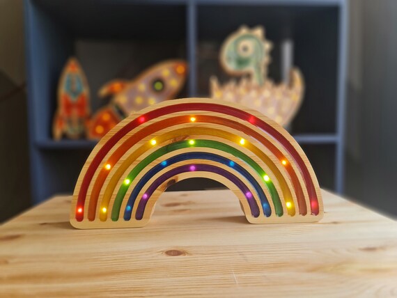 Child’s hand turning on a wooden rainbow LED light at bedtime.