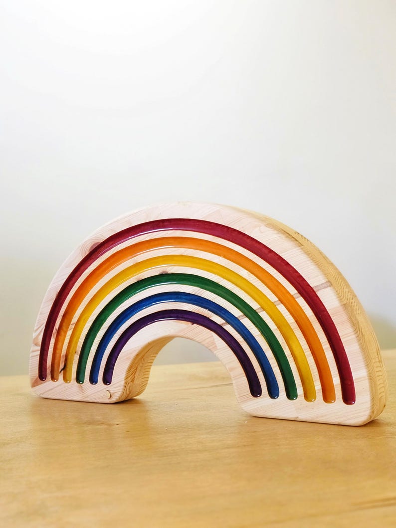 May include: Wooden rainbow toy with seven arched layers in vibrant colors: red, orange, yellow, green, blue, indigo, and violet. The toy is made of natural wood with a smooth finish, and the arches are nested together. A colorful educational toy.