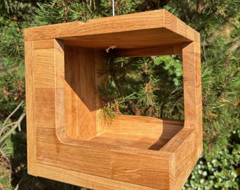 May include: A wooden bird feeder with a square shape and a rectangular opening. The feeder is made of natural wood and has a rustic look.