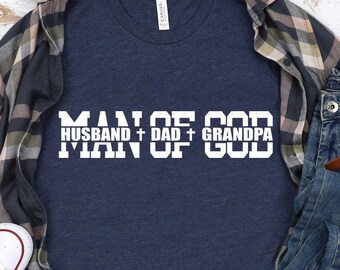 Könnte beinhalten: Ein marineblaues T-Shirt mit weißem Text, der "Man of God" lautet, wobei die Wörter "Husband", "Dad" und "Grandpa" über dem Wort "Man" gestapelt sind.