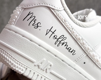 May include: White leather sneaker with pearl and rhinestone embellishments. The text "Mrs. Hoffman" is written in black script on the side. The word "AIR" is visible on the sole.