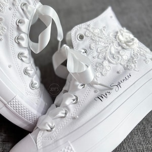 May include: White high-top sneakers with lace detailing and a satin ribbon. The shoes are personalized with the text "Mrs. Spencer".