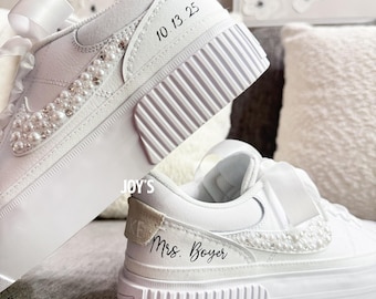 May include: White platform sneakers with pearl and rhinestone embellishments. The sneakers have a ribbon detail and the text "10.13.25" and "Mrs. Boyer". These custom shoes are perfect for a wedding or special occasion.