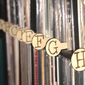 May include: A close-up of a bookshelf with wooden letter dividers. The dividers are labeled with the letters F, G, and H. The bookshelf is filled with various books and CDs.