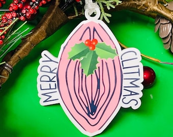 May include: A pink Christmas ornament with the text "MERRY CLITMAS". The ornament features a stylized design with holly and berries. The ornament is hanging on a green background with red berries and greenery.