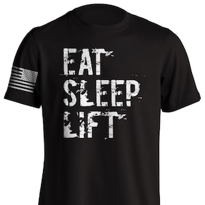 Peut inclure: T-shirt noir avec un graphisme blanc vieilli qui dit "Eat Sleep Lift" et un petit drapeau américain sur la manche gauche.