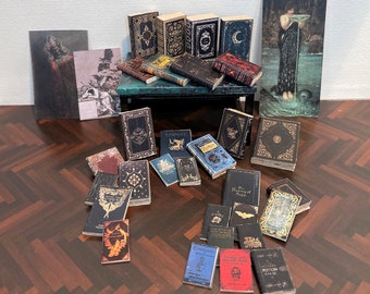 May include: A collection of miniature books with black covers and gold lettering. The books are arranged on a small wooden table with a green top. There is a framed drawing of a building above the table and a painting of a woman in a flowing gown to the right. The books have titles such as "Undine", "A History of Magic", "Curse and Hallucinations", and "The Potion Seller".