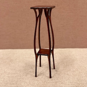 Puede incluir: Un soporte para plantas de madera marrón oscuro con una parte superior cuadrada y patas curvas intrincadas.