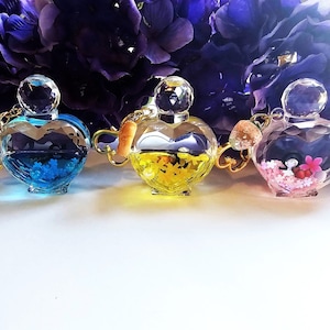 May include: Three heart-shaped glass bottles with gold chains and stoppers. The bottles contain blue, yellow, and pink glitter and small decorative items.