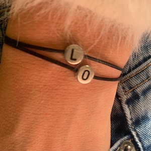 May include: A black cord bracelet with two silver beads that spell out "LO".