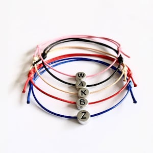May include: A set of five colourful friendship bracelets with silver beads spelling out the word "WAKBZ".