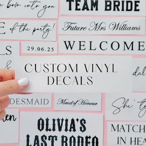 May include: A selection of white rectangular custom vinyl decals with black text, featuring phrases such as "TEAM BRIDE", "WELCOME", and "OLIVIA'S LAST RODEO". The background is a pale pink.