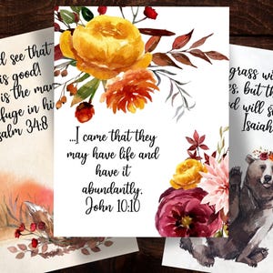 May include: Three rectangular art prints featuring watercolor floral arrangements and black script text. The center print displays John 10:10, the left print shows Psalm 34:8, and the right print features Isaiah 40:8 with a brown bear illustration.