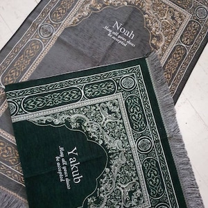 Op de afbeelding: Twee gebedskleden, &eacute;&eacute;n grijs en &eacute;&eacute;n groen, met sierlijke bloemen- en geometrische patronen. Het grijze kleed heeft de naam "Noah" en de zin "May all your duas be accepted." Het groene kleed heeft de naam "Yakub" en dezelfde zin.