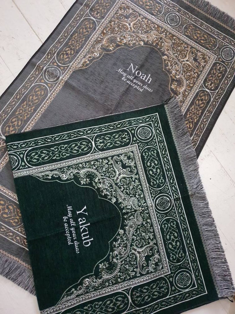 Op de afbeelding: Twee gebedskleden, &eacute;&eacute;n grijs en &eacute;&eacute;n groen, met sierlijke bloemen- en geometrische patronen. Het grijze kleed heeft de naam "Noah" en de zin "May all your duas be accepted." Het groene kleed heeft de naam "Yakub" en dezelfde zin.
