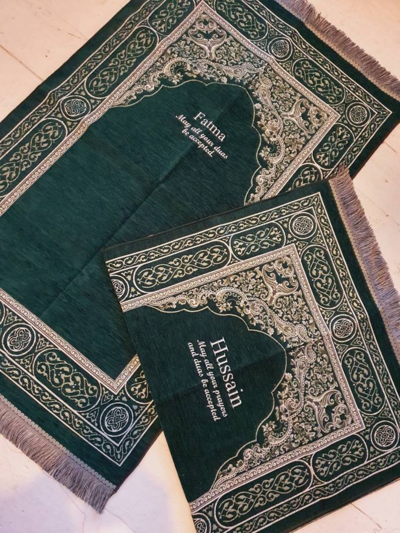 Op de afbeelding: Twee groene gebedskleden met sierlijke zilveren en gouden ontwerpen. E&eacute;n kleed is rechthoekig, de andere kleiner met een gewelfde bovenkant. Tekst op de kleden luidt "Fatma, Mogen al je dua's geaccepteerd worden" en "Hussain, Mogen al je gebeden en dua's geaccepteerd worden."