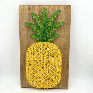 Op de afbeelding: Een gele en groene ananas string art op een houten achtergrond.