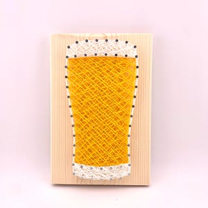May include: A wooden board with a yellow and white string art design of a beer glass.