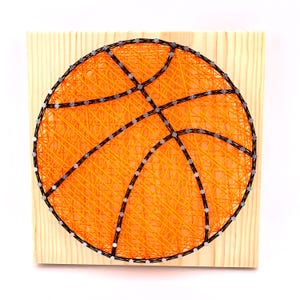 Puede incluir: Arte de hilo naranja y negro de una pelota de baloncesto sobre un fondo de madera.