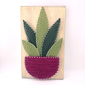 May include: String art of a green plant in a pink pot on a wooden background.
