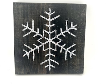 Peut inclure: Plaque carrée en bois teinté foncé avec un flocon de neige en fil blanc. Le flocon de neige est centré sur le tableau et est fait de fil blanc enroulé autour de petits clous. Le fond est en bois foncé et vieilli.