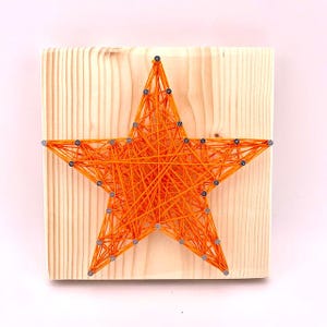 May include: Orange string art in the shape of a star on a wooden background.