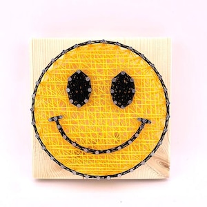 May include: A yellow smiley face made of string wrapped around nails hammered into a wooden board.
