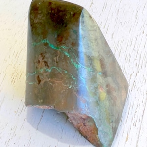 May include: A unique, irregularly shaped stone with a polished surface. The stone features a blend of earthy tones, including brown, green, and hints of blue. The surface has a marbled appearance with visible veins and textures. The stone is approximately 4 inches long.
