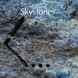 May include: Textured, multi-toned surface with the word "Skystones" in white. A dark, curved, metal object is embedded in the surface, with three small, dark holes below it. The surface has shades of blue, gray, and brown.