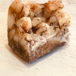May include: A natural quartz crystal cluster with a rough, textured surface. The crystal features a mix of light brown, white, and clear quartz points. The base has a darker, reddish-brown hue. This unique specimen is a decorative mineral.