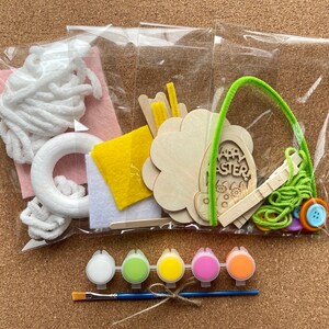 以下が含まれることがあります： イースターをテーマにしたクラフトキット。木製のカットアウト、絵の具のポット、筆、フェルトのパーツが含まれています。キットには、木製の卵のカットアウトに「Happy Easter」の文字と、緑色のパイプクリーナーのハンドルが付いています。
