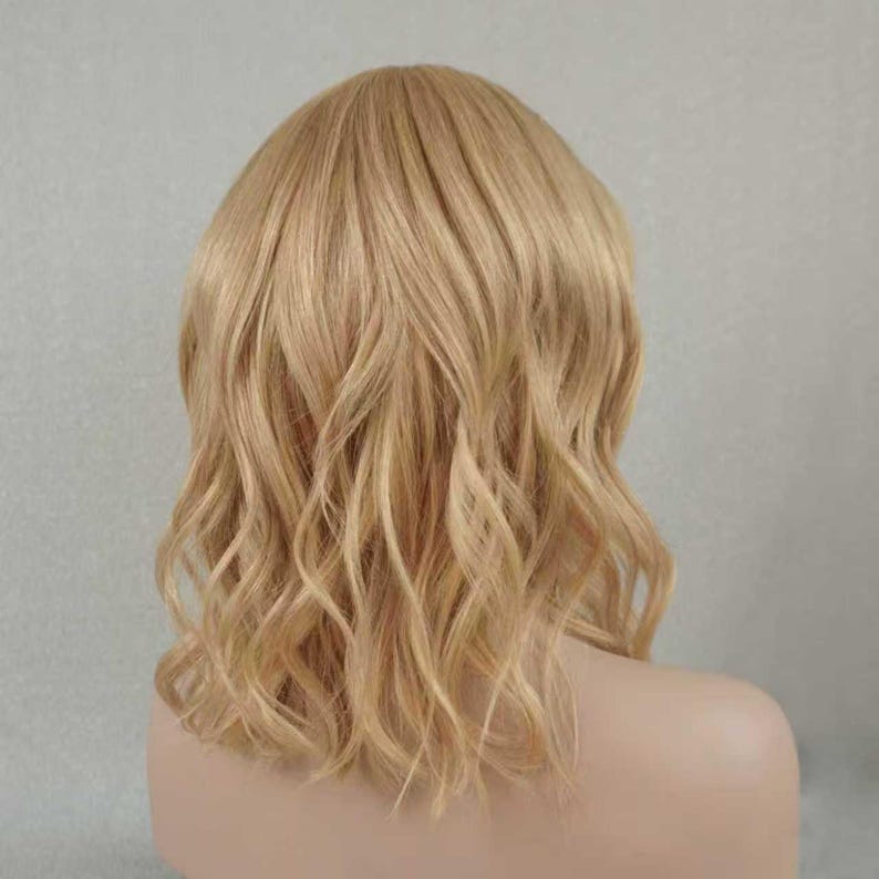 May include: A shoulder-length wig featuring wavy, light blonde hair with subtle golden highlights. The hair is styled with a soft, natural texture and a center part, falling in loose, flowing waves that frame the head and shoulders evenly.