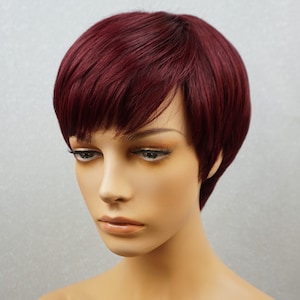 Può includere: Una parrucca corta di colore bordeaux con riga laterale e frangia. La parrucca è acconciata con un taglio pixie.