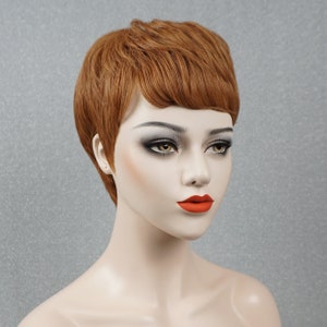 May include: A short, choppy, auburn-colored wig with a side part. The wig is styled with a fringe and is worn by a mannequin with a neutral expression.