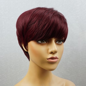 May include: A short, burgundy wig with a side part and bangs. The wig is styled in a pixie cut.