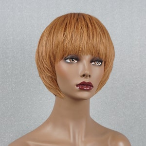 Op de afbeelding: Een kort, recht, lichtbruin pruik met een pony. De pruik is gestyled in een bob-vorm en heeft een natuurlijke, licht getextureerde look.