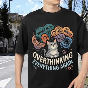 May include: Black t-shirt featuring a cartoon cat with thought bubbles. The bubbles display phrases such as "What if??" and "Too much?" The words "Overthinking Everything Again" are written below the cat in a playful font.