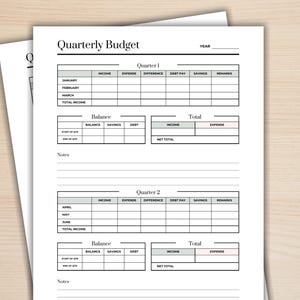 May include: Two sheets of white paper with a "Quarterly Budget" template printed on them. The template includes sections for income, expenses, savings, and debt, with space for notes. The paper is on a light wood-grain surface.